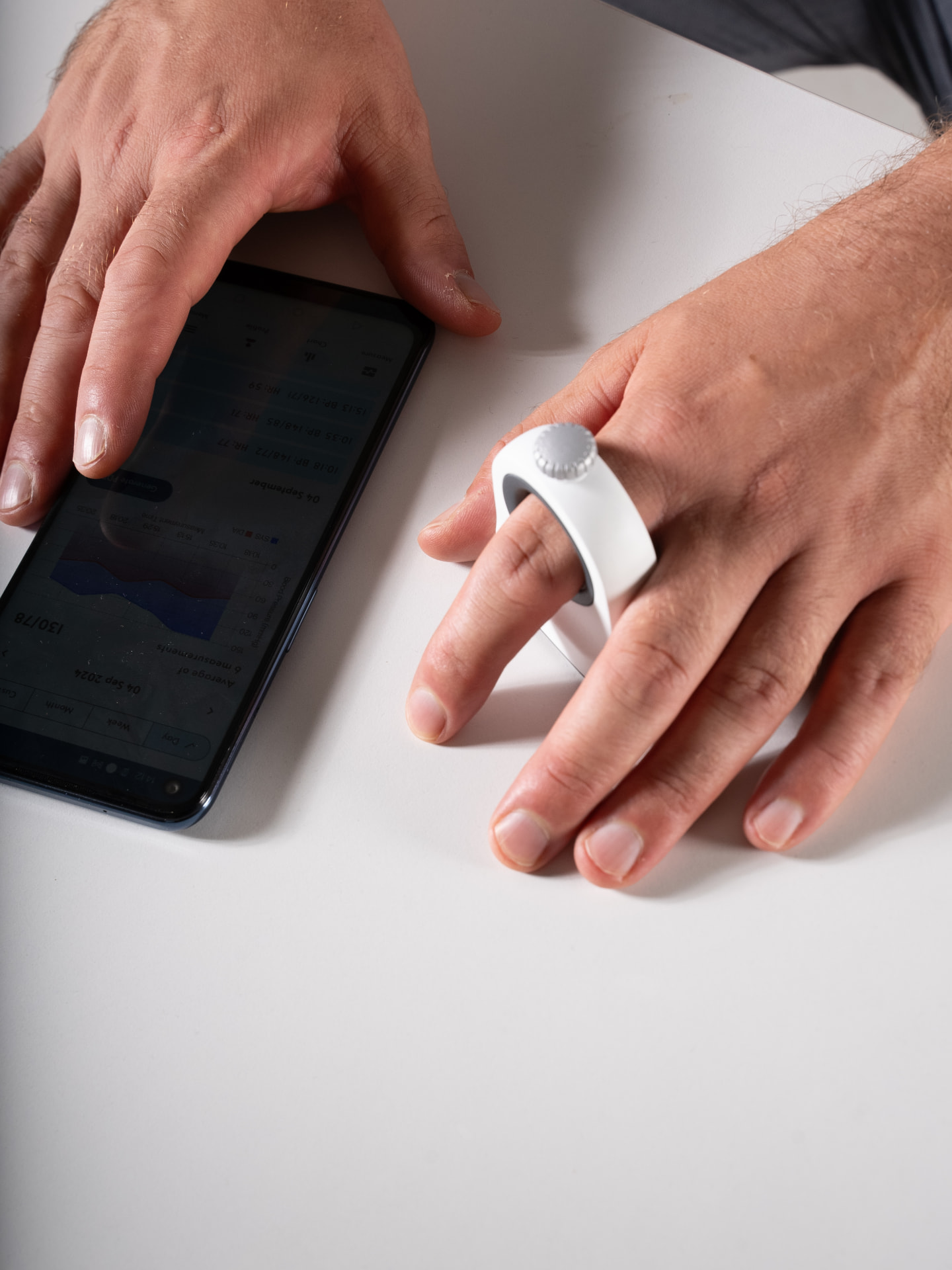 Siiring finger blood pressure monitor being used for a quick measurement alongside the companion mobile app